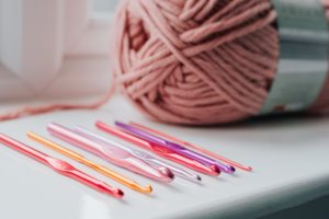 a skein of pink yarn and crochet hooks of various sizes sitting on a desk