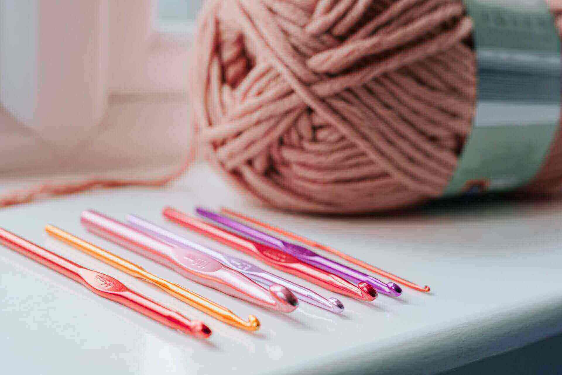 a skein of pink yarn and crochet hooks of various sizes sitting on a desk