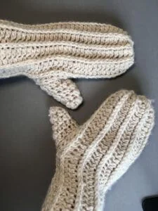 A pair of chunky white crochet mittens made with wool blend yarn.