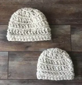 Two crocheted baby beanies in white yarn on a dark background.
