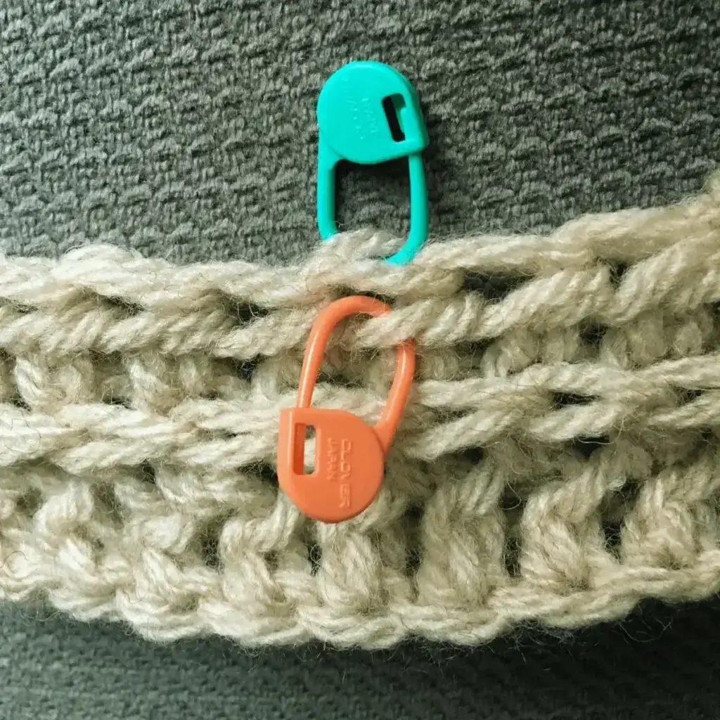 A crocheted stitch sample of half double crochet, made in white yarn. There are stitch markers inserted in the half double crochet to demonstrate the proper place to insert the crochet hook.