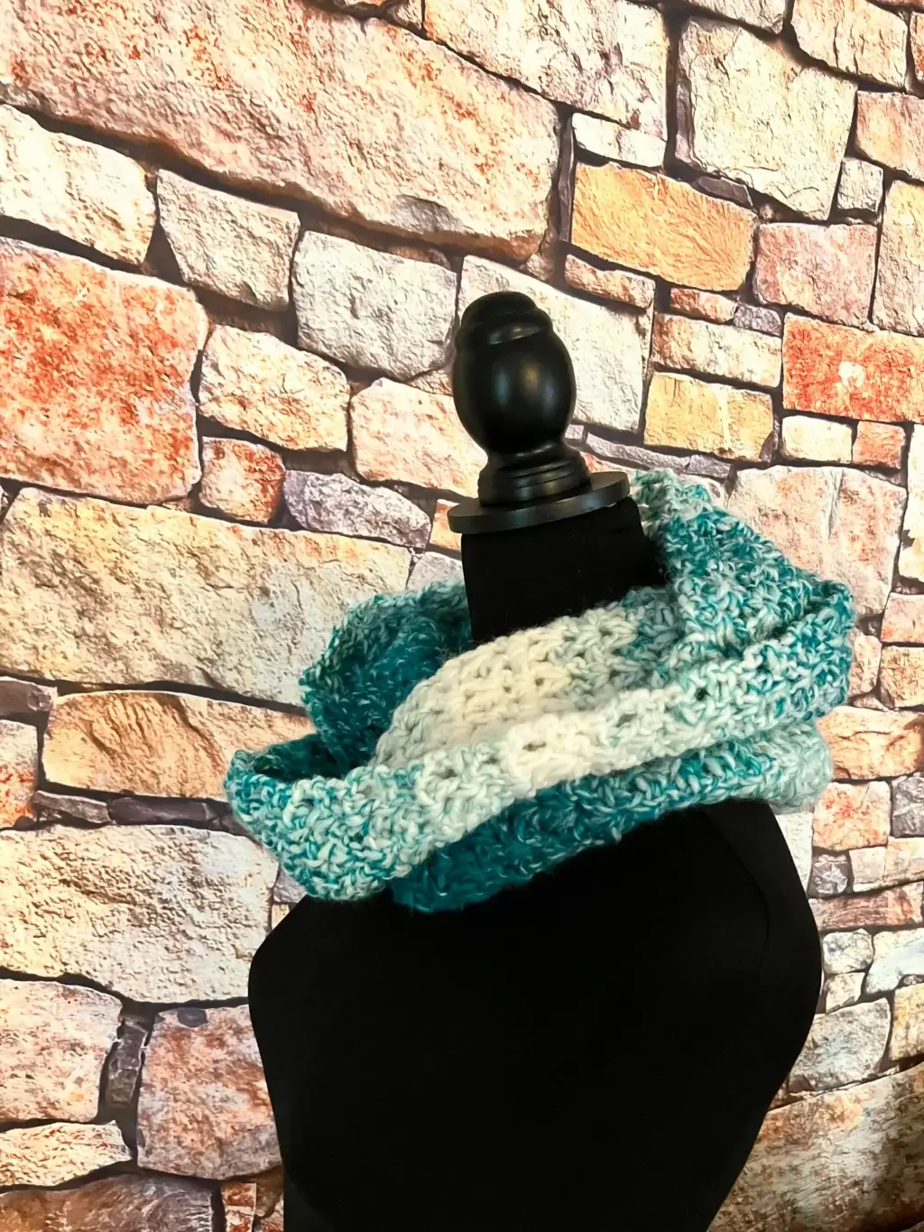 A white and teal crochet infinity scarf is displayed on a dressmaker's form.