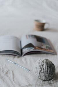 A ball of yarn and crochet hook next to an open book.
